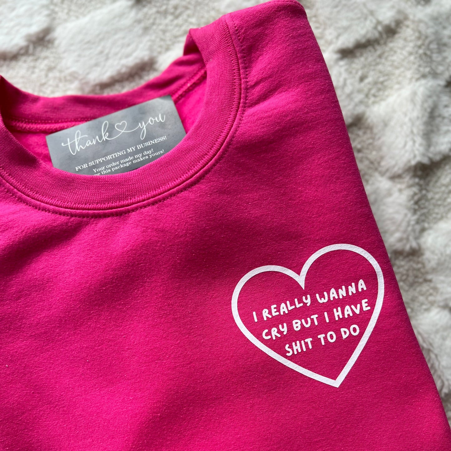 This image displays a bright pink t-shirt with the phrase "I really wanna cry but I have to do" printed in a white heart shape on the front. The text is arranged in a simple, elegant font that stands out against the vibrant fabric.