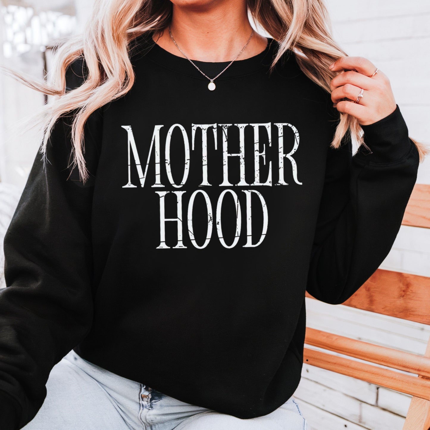 Black sweatshirt with 'MOTHER HOOD' text worn by a person, against a wooden background.