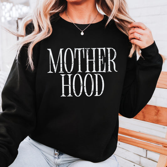 Black sweatshirt with 'MOTHER HOOD' text worn by a person, against a wooden background.