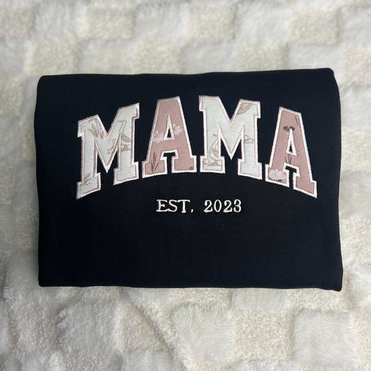 Black t-shirt with 'MAMA EST. 2023' text on a textured surface